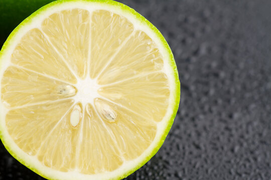 A macro close-up shot of a sliced fresh lime, displaying its segmented pulp, seeds, and green rind against a dark textured background.
