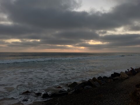 Dusky cloudy sky over the Pacific shoreline with riprap rocks along the beach during twilight, Carlsbad, California.