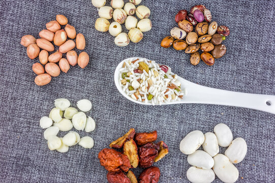 Various dried edible ingredients including grains, beans, nuts and jujubes, displayed with a spoonful of mixed grain on a textured background.