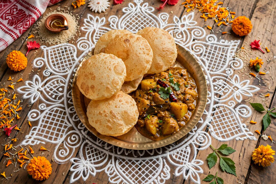 Traditional Bengali breakfast luchi and alur dom curry on brass plate with white alpona rangoli diya and marigold flowers for Durga Puja