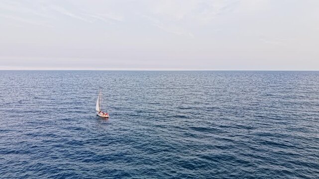 A small boat sails across the ocean under clear skies. The water is blue and stretches far into the distance. There are no landforms in sight.