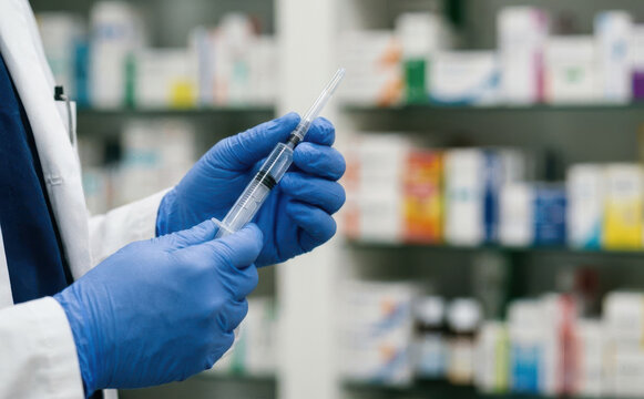 Professional doctor in blue gloves holding a medical syringe preparing a vaccine dose in a pharmacy