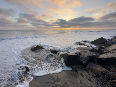 High tide surf churning water and foam against protective riprap boulders at Ponto Beach in Carlsbad, California.