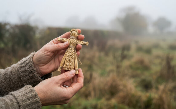 Woman holding a traditional straw corn dolly talisman in a misty field symbolizing folk craft and harvest rituals