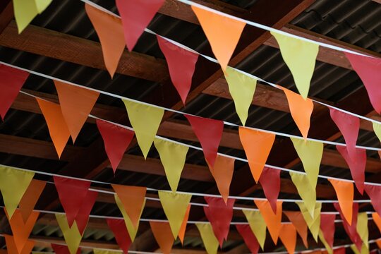 Rows of orange yellow and red triangle bunting flags hanging under a wooden roof creating a cozy autumn festival atmosphere during an outdoor event.