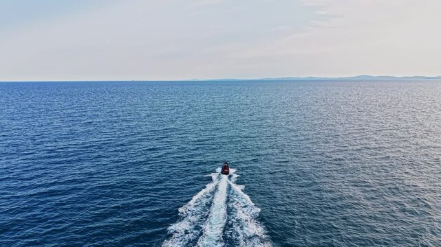 A boat moves through the blue sea, leaving wake in its path. The horizon is distant with a clear sky above. This scene shows a typical day at sea.