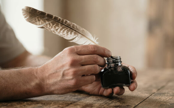 Adult man dipping a feather quill into a glass inkwell on a wooden table, representing historical writing and traditional calligraphy concepts