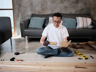 Fototapeta premium Asian mature man sitting and preparing flat-pack furniture parts and DIY equipment for self-assembly, home improvement, wooden craft installation, hobby workshop, carpentry handyman active lifestyle.