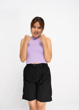 Excited Young Woman In Lavender Tank Top And Black Shorts With Clenched Fists Against A White