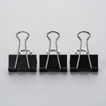 Three black binder clips lined up on a gray surface, useful for organizing papers and office supplies.