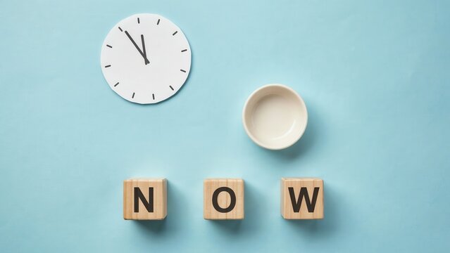Minimalist time management concept with wooden blocks spelling NOW, paper clock face on blue background, urgency and deadline metaphor