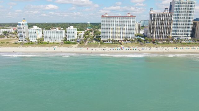 Aerial perspective of Myrtle Beach, featuring sandy shores, gentle ocean waves, and tall hotels along the coastline with a bright sky