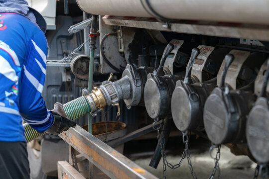 Fuel tanker operator connecting a heavy-duty flexible discharge hose to the truck's fuel transfer valve.