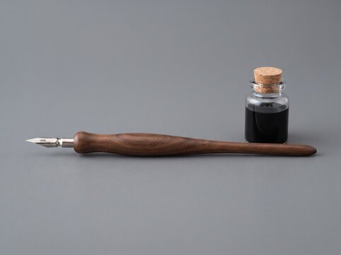 Elegant wooden calligraphy pen with a small glass ink bottle on a neutral grey studio background