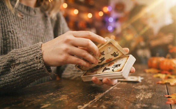 Young adult woman shuffling Halloween cards at a wooden table in a cozy indoor setting