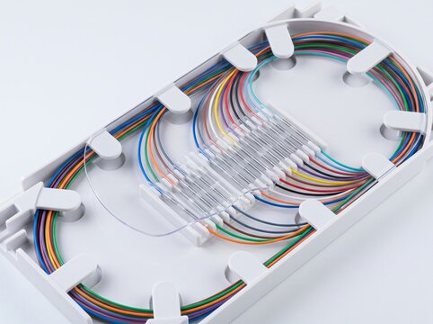 Scientific macro photograph of cleanroom fiber optic fusion splice organizer tray holding neatly routed silica glass optical fibers with clear micro heat shrink protective sleeves in telecom rack