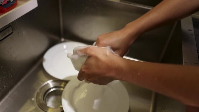 Woman Washing Dishes with Soapy Sponge in Kitchen Sink