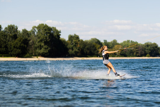 Female wakeboarder wakesurfing. Girl riding waterski cabel. Holding tow rope. Summer activities in the lake.