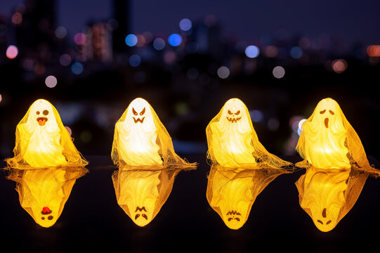 Halloween glowing ghost decorations lined up with reflections against a city skyline at night.