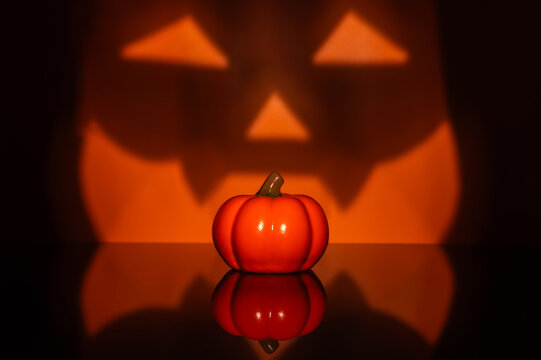 Halloween pumpkin with a glowing jack o lantern face and reflection on a black background.