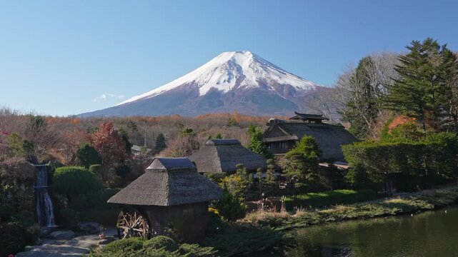 Snow-capped Mount Fuji rises above thatched village roofs and gardens.