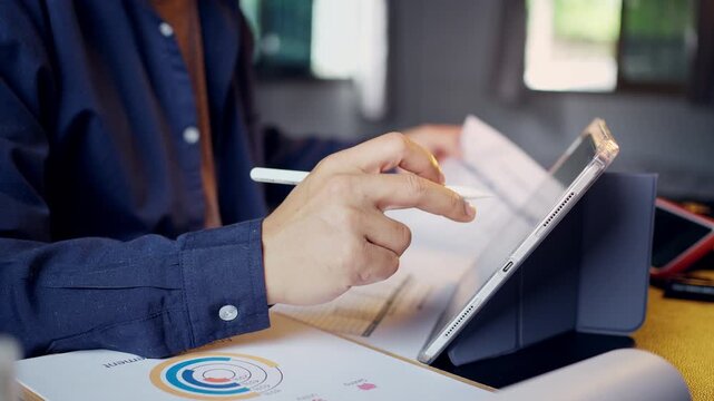 Businessman holding a paper document and cross-referencing data with a digital tablet at his office desk.