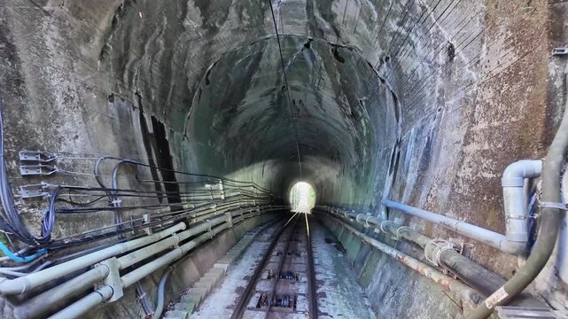 Camera tracks along railway tracks through a dim concrete tunnel.