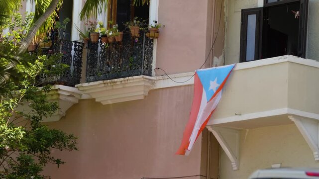 The flag of Puerto Rico is displayed from a balcony at Old San Juan, surrounded by plants, showcasing local culture and pride. Camera moves in natural hand held motion.