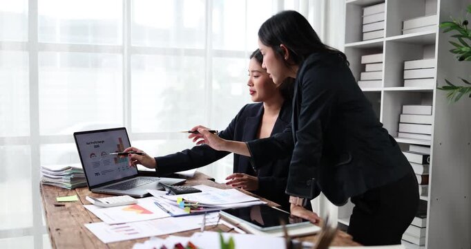 Two young businesswomen collaborating on financial data analysis, discussing corporate strategy and reviewing charts during a productive office meeting, focusing on growth and success