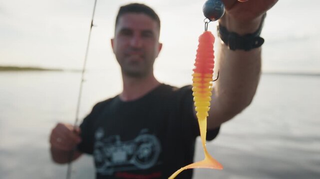 Angler stands in the boat and shows fishing lure on the camera