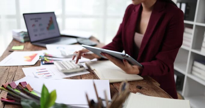 Businesswoman analyzing financial reports and accounting data, using a calculator and digital tablet for strategic planning and economic success in the modern office