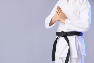 Young man with black belt practicing karate on light background © Pixel-Shot