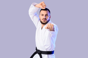 Young man with black belt practicing karate on light background © Pixel-Shot