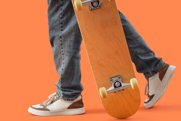 Legs of young man with skateboard on orange background, closeup © Pixel-Shot