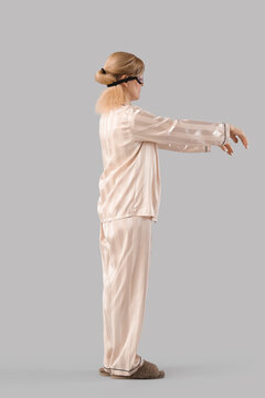Female sleepwalker in pajamas on grey background