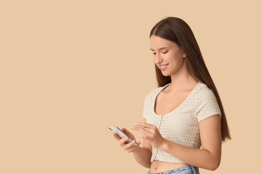 Beautiful young woman with modern mobile phone on beige background