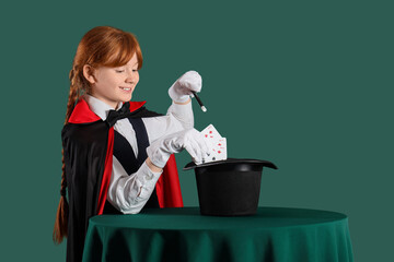 Young magician showing magic trick with playing cards and hat on table against green background © Pixel-Shot