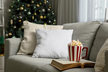 Fototapeta premium Cup of cocoa with book on sofa in living room, closeup. Christmas celebration