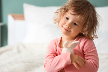 Fototapeta premium Cute little girl hugging toy bunny in bedroom, closeup