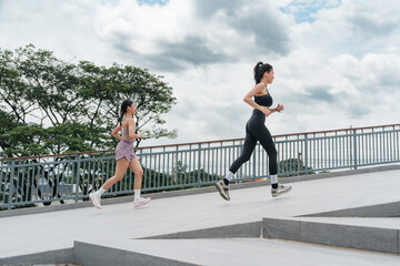 Fototapeta premium Two Asian women running outdoors on bridge for fitness and healthy lifestyle