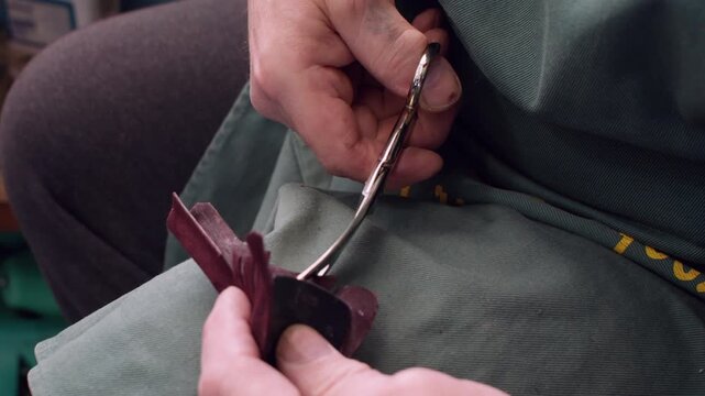 Handmade occupation. Cobbler workplace. Unrecognizable craftsman hands using leather material scissors for footwear manufacturing.