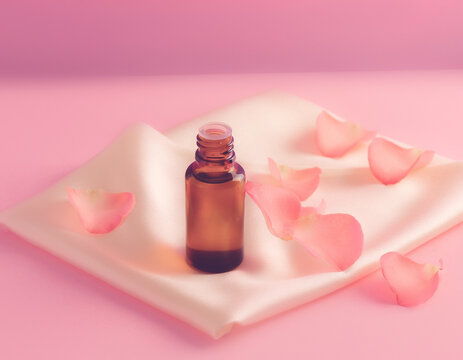 A glass bottle of essential oil placed on a soft pink silk fabric with rose petals.