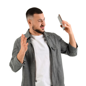 Young man with mobile phone suffering from loud noise on white background