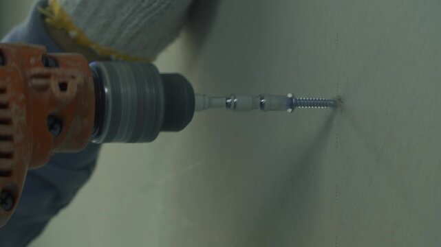 Gloved hand aiming a screwdriver bit at a drywall sheet