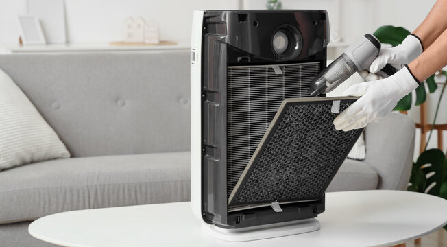 Air purification and home maintenance, person cleaning air purifier filter with handheld vacuum to improve indoor air quality and remove dust particles
