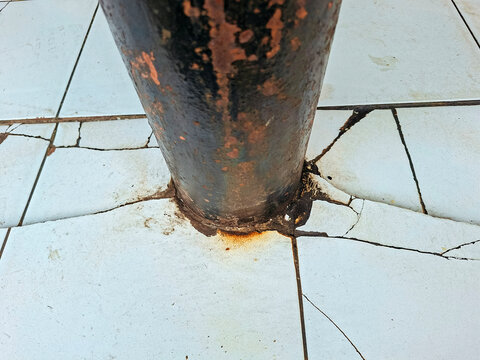 A rusty metal pole base fixed onto a cracked tiled floor surface