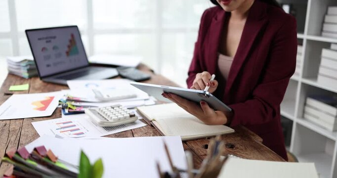 Businesswoman analyzing financial reports and accounting data, using a calculator and digital tablet for strategic planning and economic success in the modern office