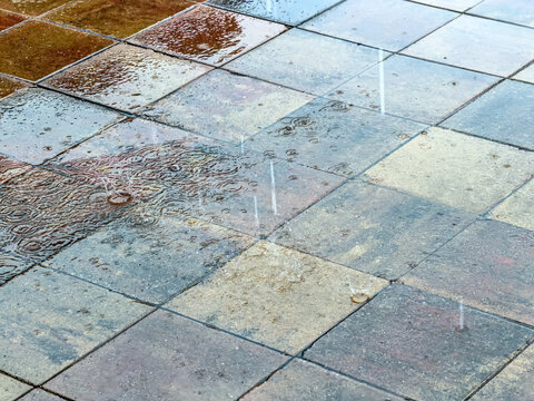 sidewalk in city street during rain. wet brown tiled pavement blocks reflect gloomy sky.