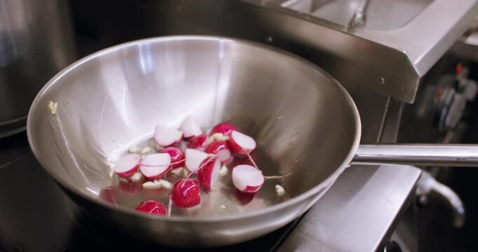 Culinary process. Frying radish. Preparing cut fresh vegetable with chopped garlic on boiling oil metal pan cooking tasty spicy hot dish.