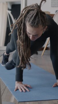 Young woman in sportswear doing physical exercise working out at home taking part in virtual sports training looking at laptop screen at home. Wellness and modern technology concept.